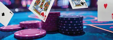 Playing cards and casino chips on a blue poker table, with a bokeh background of a casino floor.