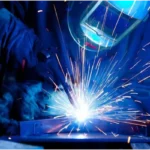 A welder wearing protective gear uses a bright, sparking welding torch on a metal workpiece.