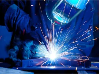 A welder wearing protective gear uses a bright, sparking welding torch on a metal workpiece.