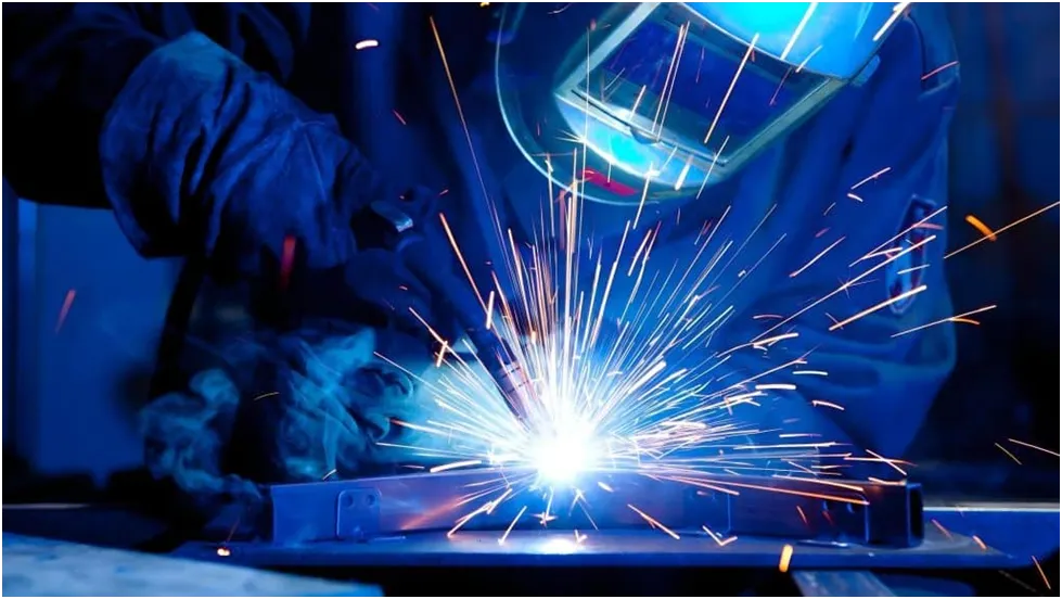 Close-up of a fiber laser welding operation with bright sparks and a blue-tinted welding mask visible.