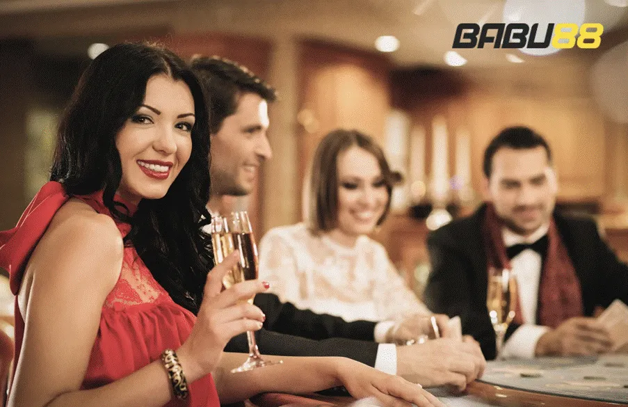 A group of stylish friends at a casino table, enjoying drinks and each other's company, potentially engaging in mobile casino gaming, with the "BABU88" logo visible.