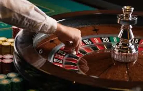 A croupier's hand launching a small white ball into a spinning roulette wheel, while colorful casino chips are visible in the background.