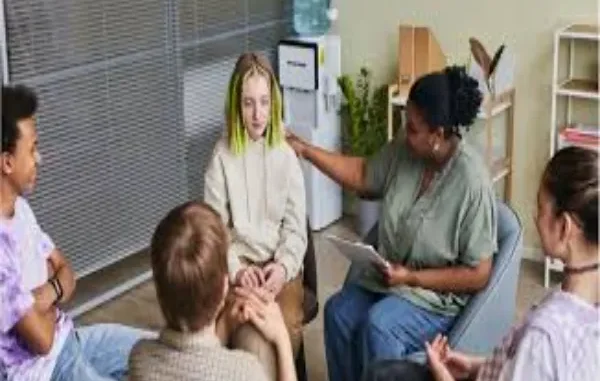 Teen Addiction Support Group A diverse group of teenagers sits in a circle with a therapist in a support group setting.
