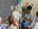 A diverse group of teenagers sits in a circle with a therapist in a support group setting.