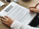 A person's hands are shown signing a "Settlement Statement" document with an orange pen, indicating the finalization of a legal or insurance agreement.