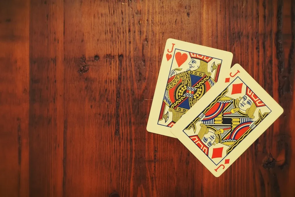 Two playing cards, a Jack of Hearts and a Jack of Diamonds, on a rustic wooden table.