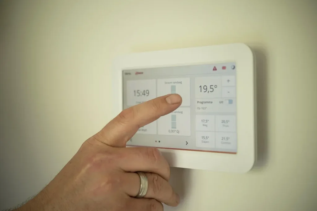 A hand adjusts a modern smart thermostat mounted on a wall, showing the digital interface for controlling home temperature and other settings.