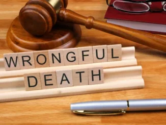 Wooden letter tiles spelling out "WRONGFUL DEATH" are placed in front of a gavel and a red book, symbolizing the legal and judicial process for wrongful death cases.