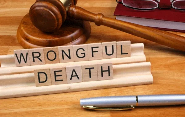 Wooden letter tiles spelling out "WRONGFUL DEATH" are placed in front of a gavel and a red book, symbolizing the legal and judicial process for wrongful death cases.
