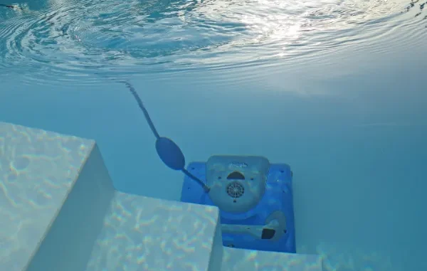 Underwater Intelligence: Aiper's Robotic Revolution in Pool Cleaning An underwater view of a bright blue robotic pool cleaner resting on the steps of a clean, white swimming pool, with sunlight shimmering on the water's surface.