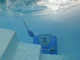An underwater view of a bright blue robotic pool cleaner resting on the steps of a clean, white swimming pool, with sunlight shimmering on the water's surface.