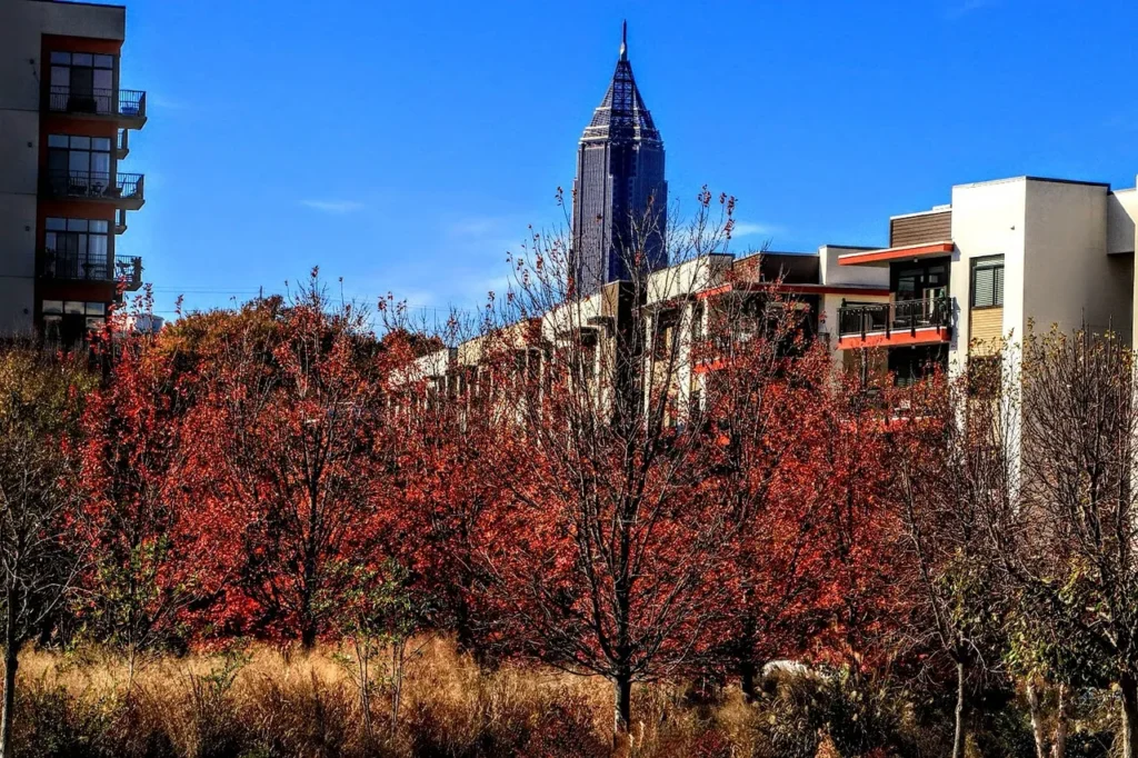 The iconic Bank of America Plaza skyscraper in downtown Atlanta, Georgia, rises above a vibrant autumn landscape of red and orange trees, with modern residential buildings in the foreground.