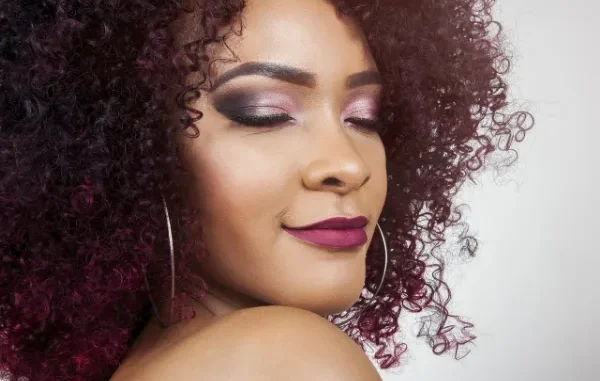 Ultimate Texture: Showcasing Burmese Curly Hair and Flawless Beauty A close-up, high-fashion portrait of a woman with vibrant, deep plum-colored, tightly coiled curly hair and dramatic eye makeup, looking over her shoulder with her eyes gently closed.