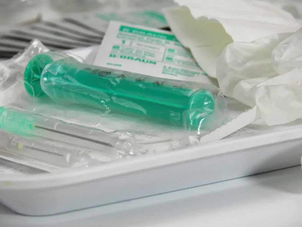 A close-up of a sealed, packaged green syringe and hypodermic needles lying on a white medical tray, representing veterinary medical supplies.