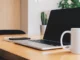 A side-angle shot of a minimalist wooden desk with an open laptop, a smartphone, and a white mug, symbolizing a modern, interconnected workspace.
