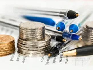 Stacks of silver and gold coins next to several pens on a printed document, symbolizing financial planning.