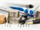 Stacks of silver and gold coins next to several pens on a printed document, symbolizing financial planning.