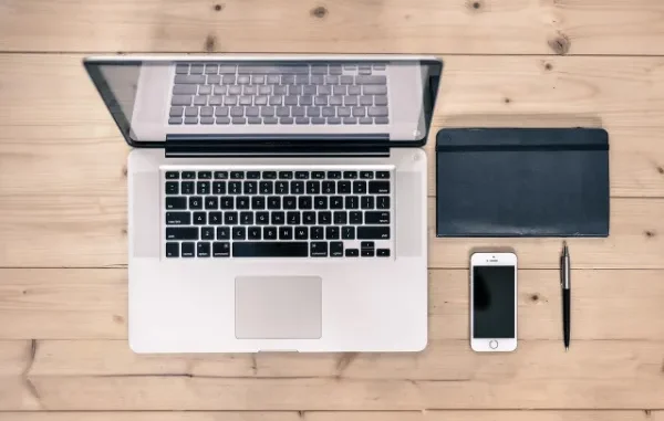 Your Workspace Connected: Network Setup & Troubleshooting for Windows 10 & 11 An overhead shot of a light wooden desk featuring an open laptop, a black notebook, a white smartphone, and a pen, representing a modern computing workspace.