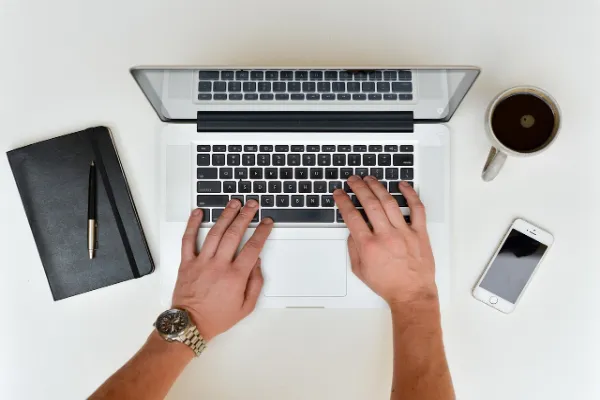 A low-angle shot of a laptop with a black screen next to a white mug and a smartphone on a light wood desk, representing a PC environment.
