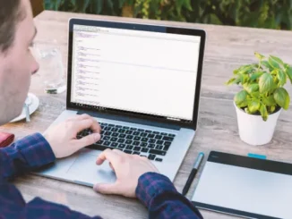 An over-the-shoulder shot of a person sitting outdoors and working on a laptop, with the screen displaying lines of code, symbolizing web development and design work using HTML templates.