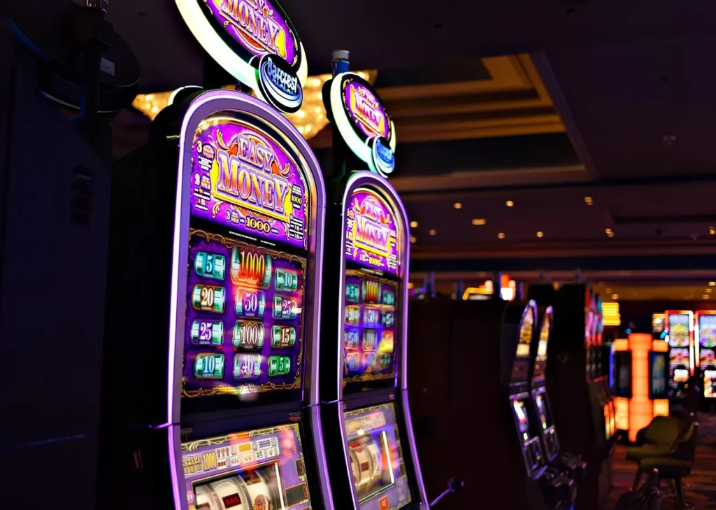 A dark casino floor with bright purple and pink illuminated slot machines, showing "Easy Money" graphics, representing the context of high-stakes gambling and financial deposits.