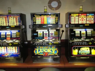 A row of three brightly lit, electronic slot machines in a casino setting, showing various credit and payout displays, symbolizing the excitement and variety of new online slot game releases.