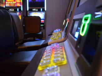 A close-up, low-angle shot of a row of modern slot machines in a dimly lit casino, featuring glowing colorful buttons and leather seating.