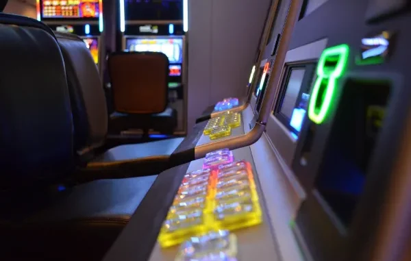 A close-up, low-angle shot of a row of modern slot machines in a dimly lit casino, featuring glowing colorful buttons and leather seating.