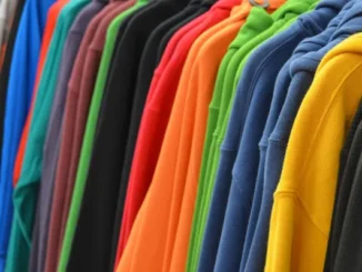 A row of vibrant, multi-colored hooded sweatshirts hanging neatly on a clothing rack, showing various fabric textures.