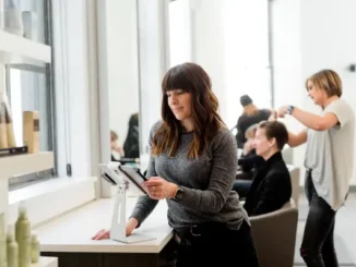 A female small business owner in a modern hair salon looking at a tablet on a stand, representing the challenges of managing local business lead generation and digital marketing.