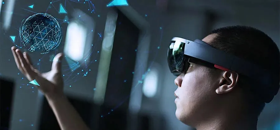 A person wearing a sleek Augmented Reality (AR) headset, reaching out to interact with a glowing, digital holographic globe floating above their hand. The image illustrates the immersive, interactive bridge between physical reality and digital gaming environments.