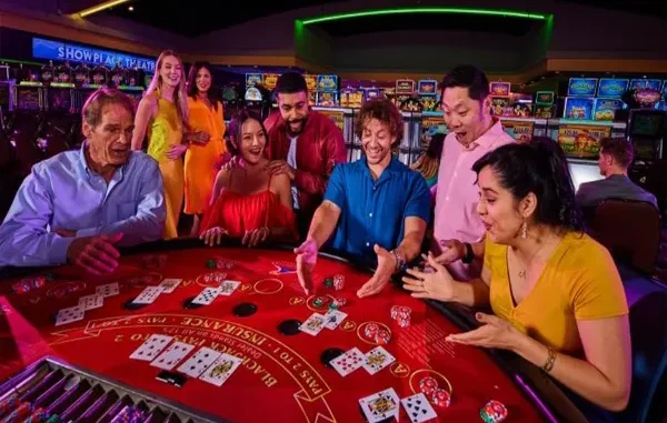 A diverse group of excited friends playing blackjack at a brightly lit casino table with cards and chips visible.
