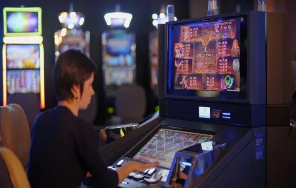 A woman sitting at a modern slot machine in a casino, focusing on the digital screen displaying game symbols, payout multipliers, and "10 Free Games" bonus information.