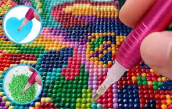 A close-up of a pink ergonomic diamond painting pen being used to place a green resin drill onto a colorful canvas. Two circular insets show the pen dipping into blue wax and picking up drills from a tray.