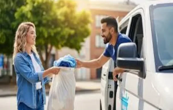 A smiling woman handing a white bag of laundry to a delivery professional in a white van on a sunny street.