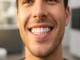 Close-up of a man with a bright, symmetrical, and natural-looking smile following an E-Max veneer procedure.
