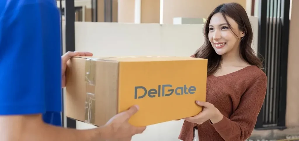 A smiling woman receives a cardboard package branded with "DelGate" from a delivery person in a blue uniform.