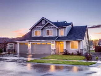 Exterior of a two-story gray suburban house at sunset with visible white gutters and downspouts directing water away from the concrete foundation.