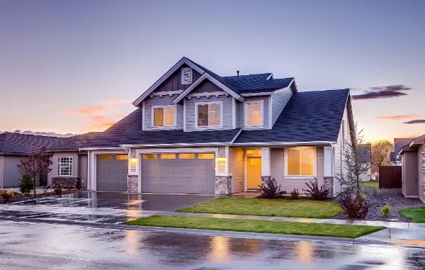 Exterior of a two-story gray suburban house at sunset with visible white gutters and downspouts directing water away from the concrete foundation.
