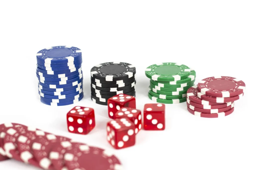 A clean, high-angle shot of stacks of blue, black, green, and red poker chips alongside several red transparent dice on a white background.