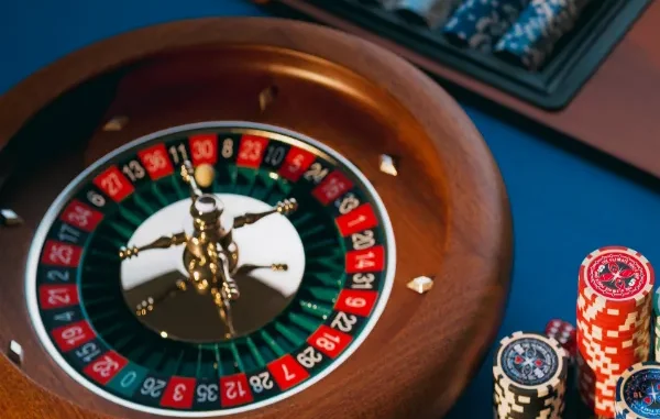 A high-angle, close-up shot of a spinning wooden roulette wheel with a white ball in motion, next to stacks of poker chips on a blue felt table.