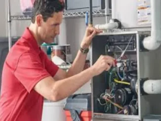 A professional HVAC technician in a red shirt inspecting the internal wiring and components of a residential furnace.