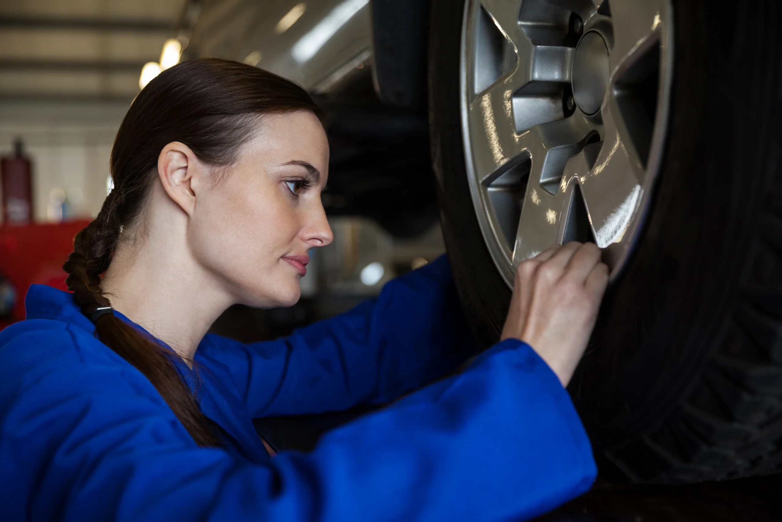 A Tesla Model 3 on a professional four-wheel alignment rack with digital laser sensors attached to the wheels for precision tracking.