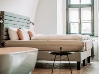 A modern bedroom setup showing a light-colored bed with a teal upholstered headboard and two pink custom-designed throw pillows, illustrating easy home decor options for non-designers.