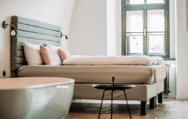 A modern bedroom setup showing a light-colored bed with a teal upholstered headboard and two pink custom-designed throw pillows, illustrating easy home decor options for non-designers.