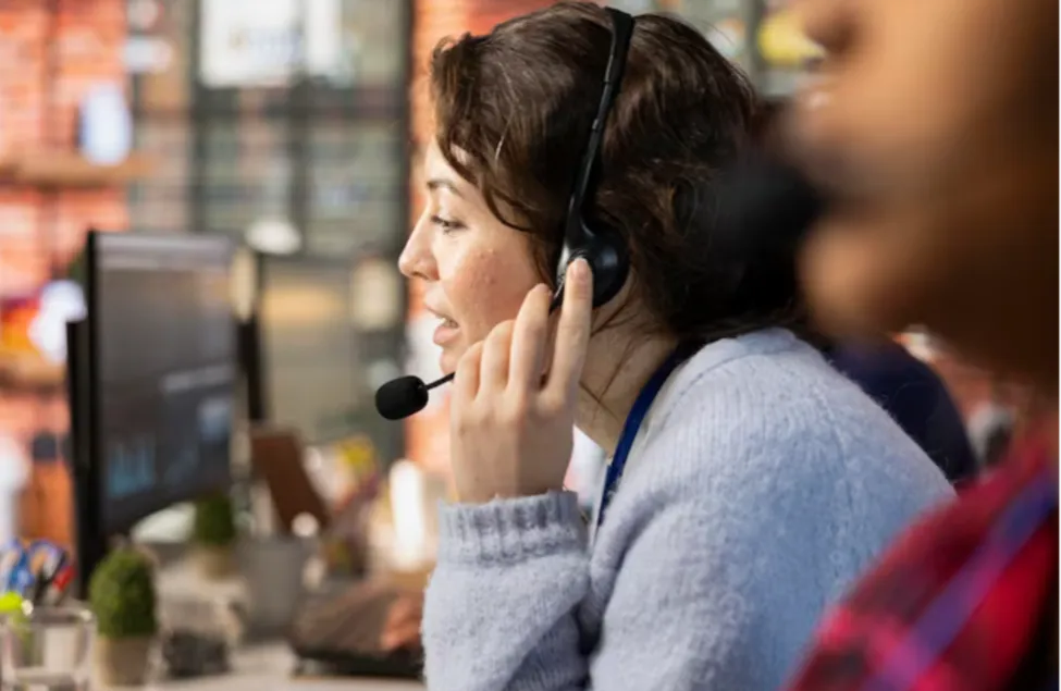A professional female support agent wearing a headset and speaking into a microphone while working in a modern, high-tech inbound call center environment.