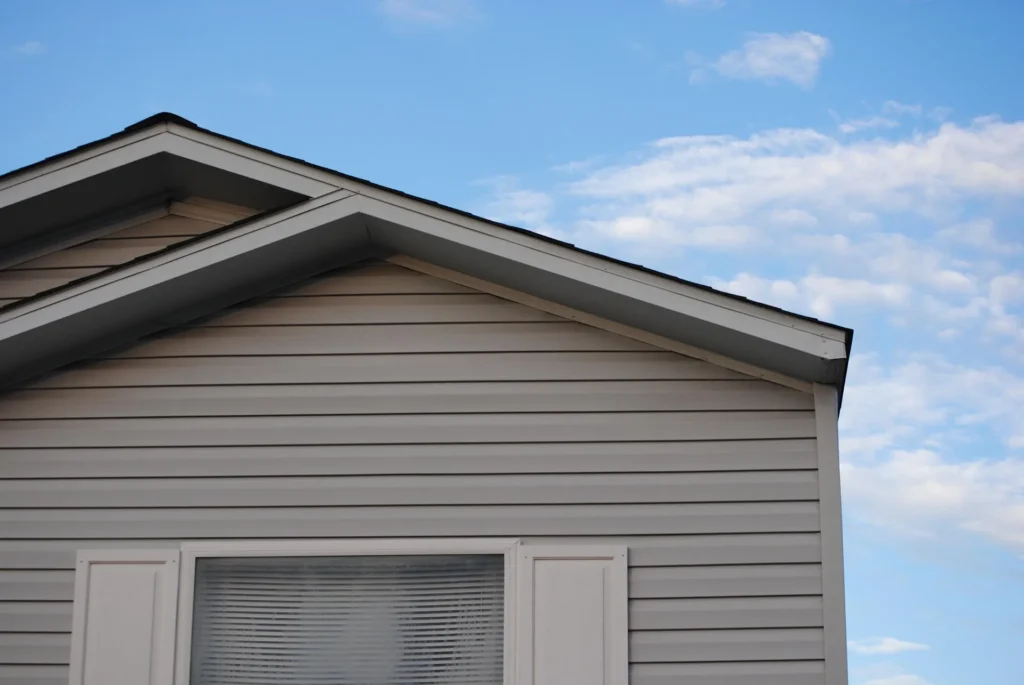 A close-up view of a well-installed grey shingle roof and vinyl siding on an Austin home under a blue sky, showcasing professional craftsmanship.