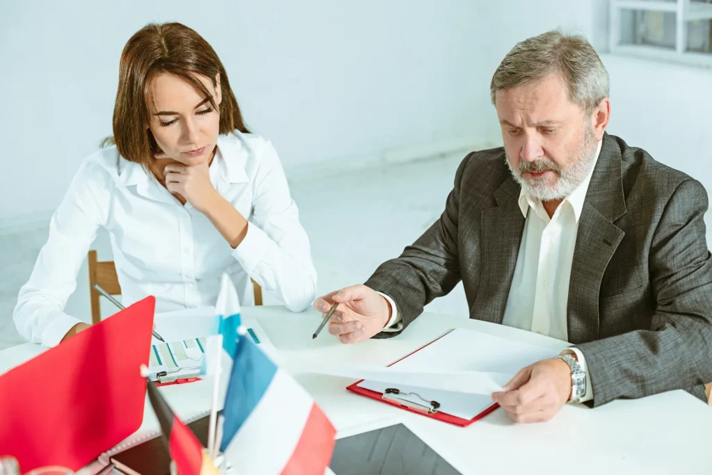 A professional bankruptcy attorney in a gray suit reviewing financial documents and charts with a concerned client at a white desk.