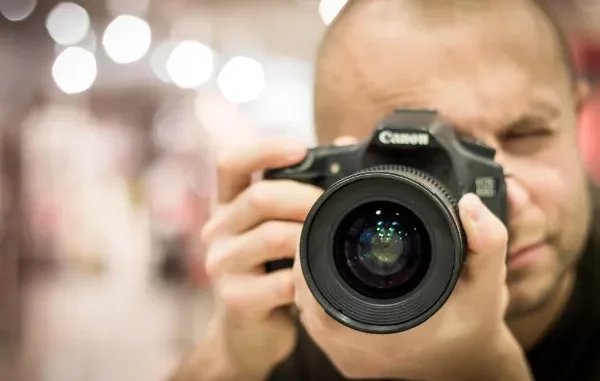 A professional photographer holding a DSLR camera, illustrating a complex subject with fine details like hair and equipment that test the precision of AI background removal tools.