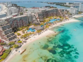 High-angle aerial view of a luxury beachfront resort in Cancun, featuring turquoise Caribbean waters, white sand beaches, and the Nichupté Lagoon in the background.
